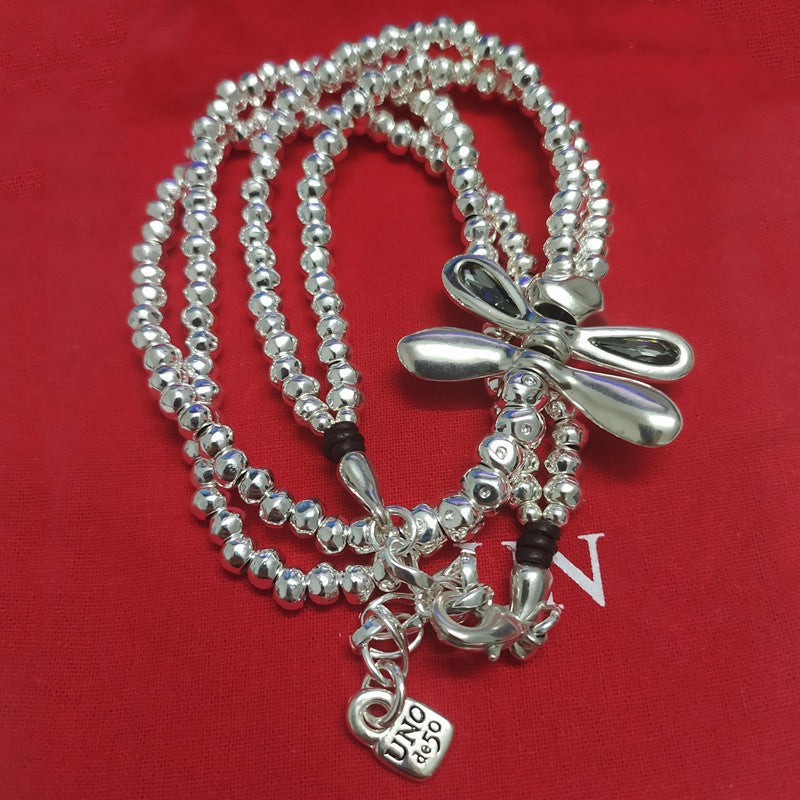 Silver beaded necklace with dragonfly and heart charm on a red background