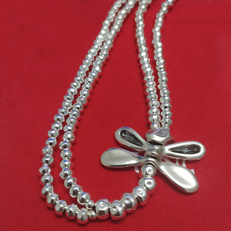 A silver beaded necklace with a bow-shaped pendant, displayed on a textured red background.