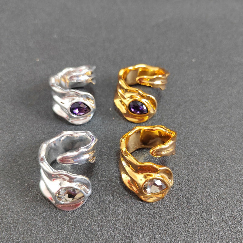 Four twisted wrap-style rings arranged on a dark gray surface, including two silver-toned rings with purple gemstones and two gold-toned rings with clear faceted gemstones.