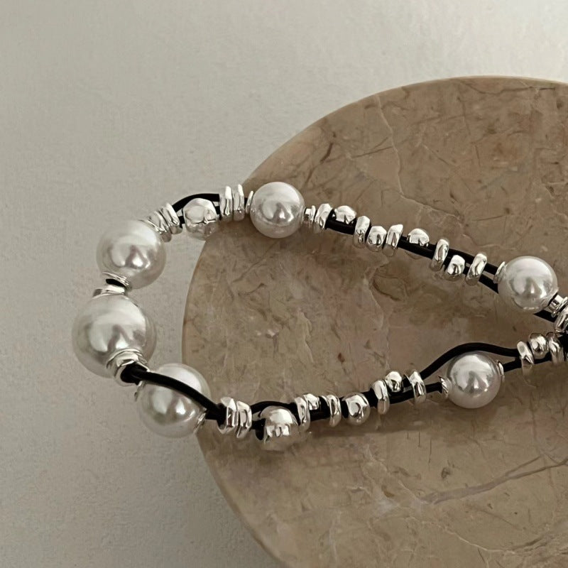 A beaded bracelet with large white faux pearls and polished silver spacer beads, draped over a round beige stone coaster against a light neutral background.
