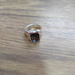 A silver-toned ring with a rectangular dark gemstone, resting on a brown wooden surface.