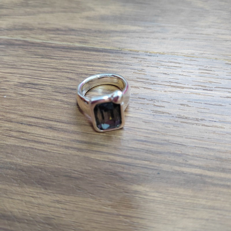 A silver-toned ring with a rectangular dark gemstone, resting on a brown wooden surface.