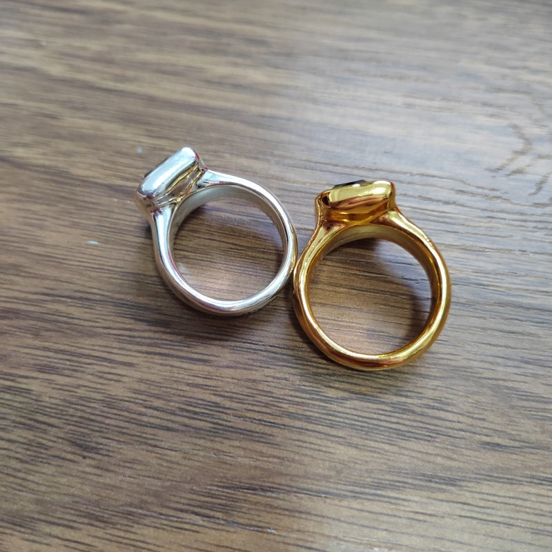 Two bezel-set rings, one in polished silver and one in polished yellow gold, displayed side-by-side on a dark wood grain surface.