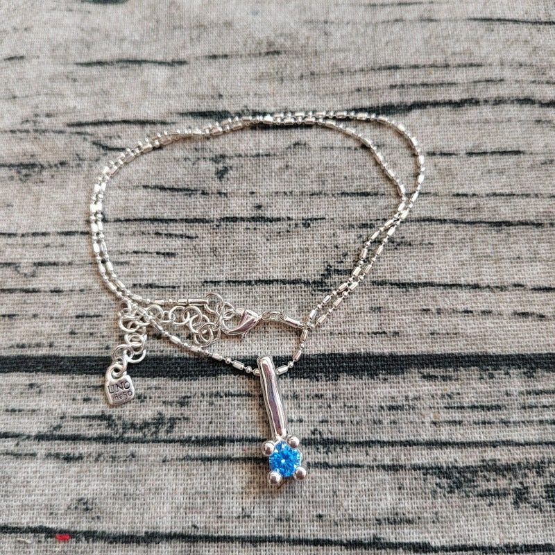 Silver bracelet with a blue gemstone charm on a textured surface