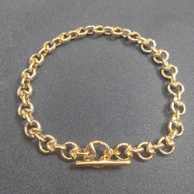 A gold chain bracelet with a toggle clasp, displayed on a dark gray textured surface.