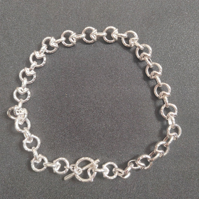 A silver chain bracelet with interlocking oval links and a toggle clasp, displayed on a dark textured background.