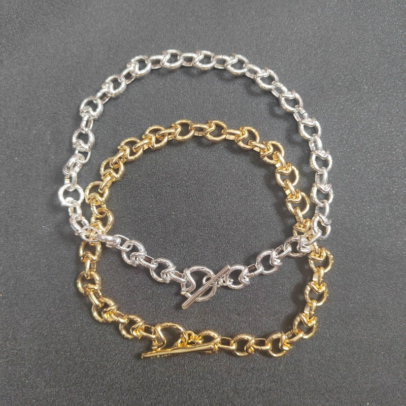 Two delicate chain bracelets, one in silver-tone metal and one in gold-tone metal, featuring alternating links and toggle clasp closures, displayed on a dark gray textured background.