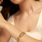 A close-up lifestyle shot of a model wearing a gold chain bracelet with textured chevron links over a cream-colored satin top.