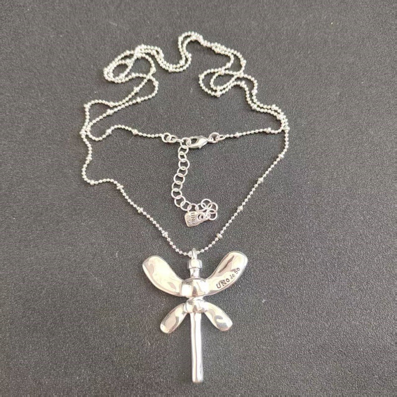 A sterling silver dragonfly pendant necklace with a delicate ball chain, displayed on a dark gray textured background.
