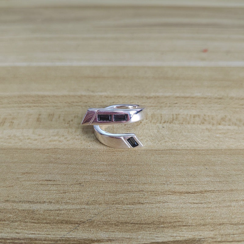 A silver wrap ring with two rectangular dark red gemstone inlays, resting on a light wood grain surface.