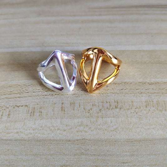 Two abstract triangular open ring earrings in polished silver and gold finishes, displayed side-by-side on a light wood grain surface.