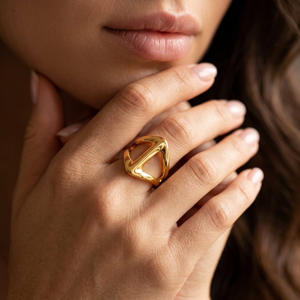 A close-up of a woman's hand wearing a chunky, geometric gold ring with a triangular openwork design.