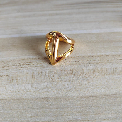 A polished gold triangular ring with an open, geometric design, resting on a light beige wood-grain surface.