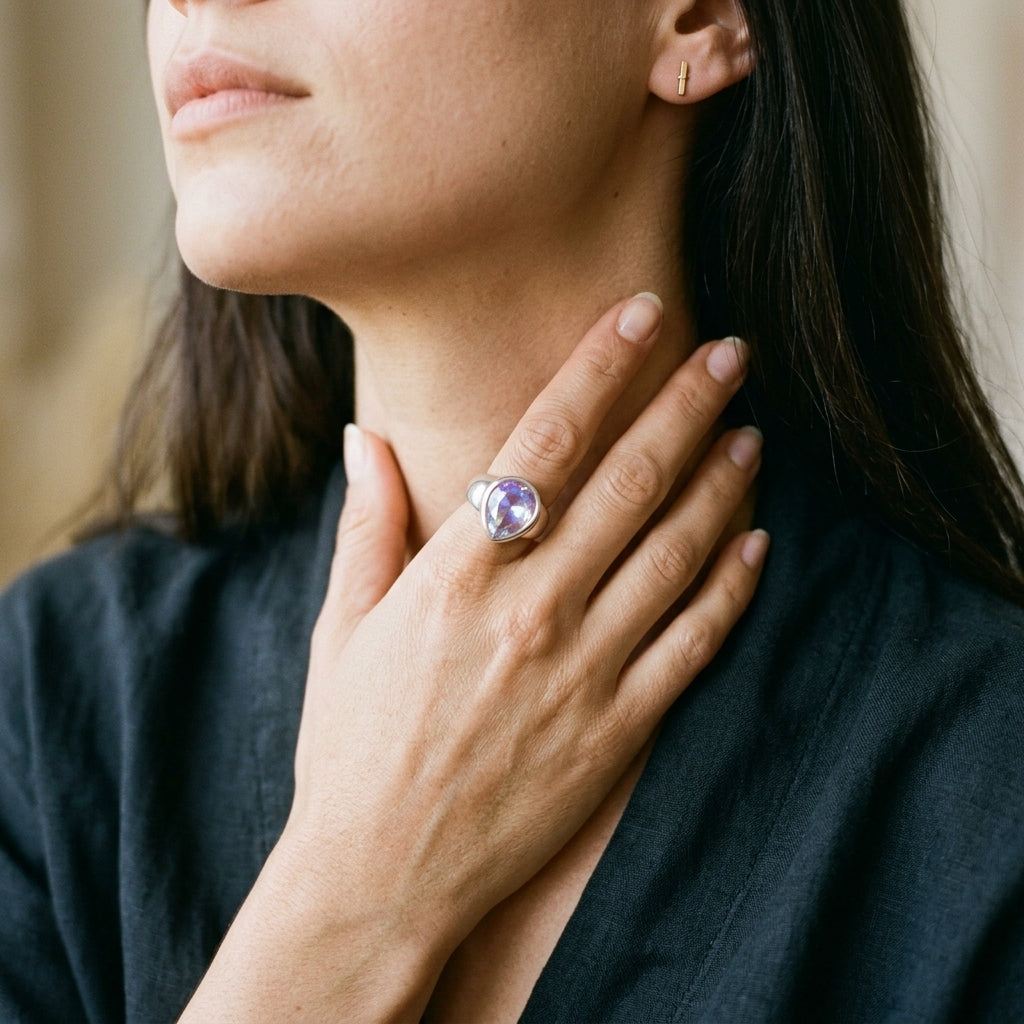 A close-up lifestyle shot of a woman wearing a silver ring with a heart-shaped purple gemstone, resting her hand on her chest.