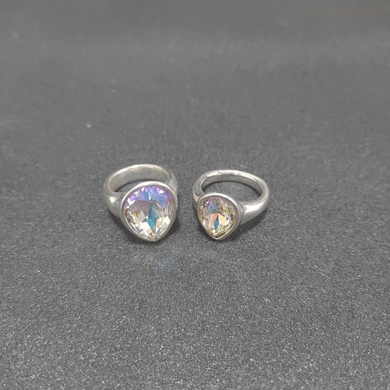 Two silver rings with heart-shaped iridescent gemstones, displayed side-by-side on a textured dark gray surface.