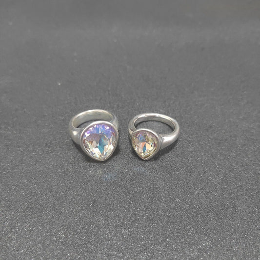 Two silver rings with heart-shaped iridescent gemstones, displayed side-by-side on a textured dark gray surface.