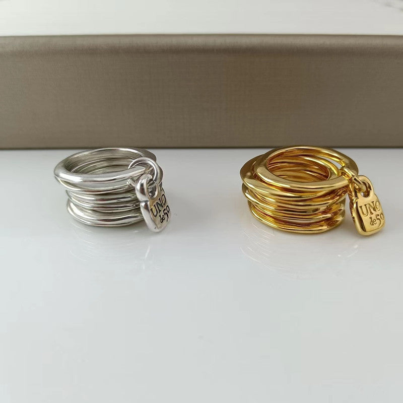  Multi-row ring on neutral background showing stacked bands and charm. Alt: “UNOde50 Multi-Row Ring with a Charm – Silver Stacked Ring.”

