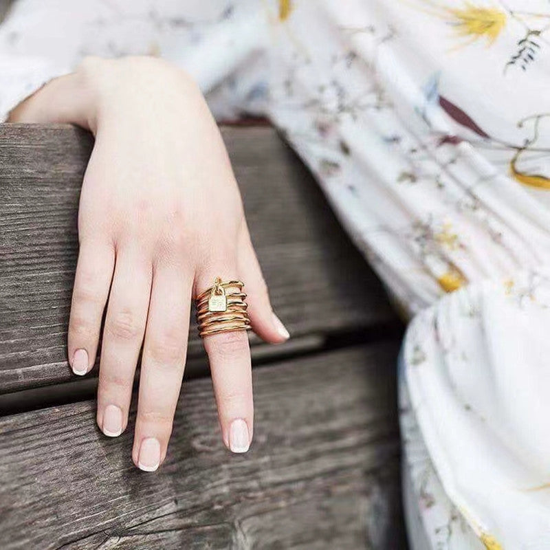  Multi-row ring on neutral background showing stacked bands and charm. Alt: “UNOde50 Multi-Row Ring with a Charm – Silver Stacked Ring.”

