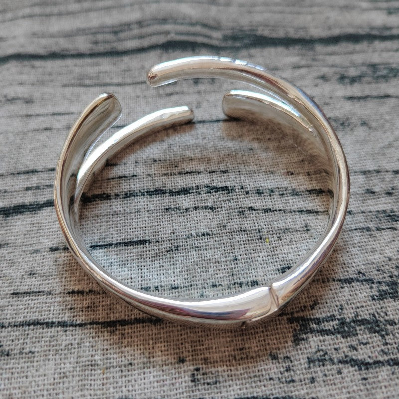 A polished silver-toned open cuff bracelet resting on a textured gray fabric background.