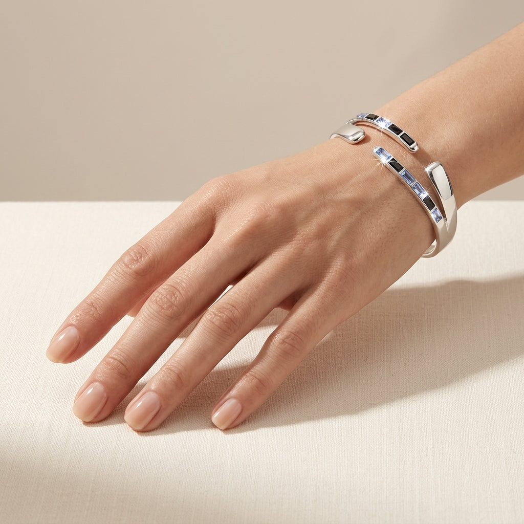A close-up of a woman's hand wearing two silver cuff bracelets with black and white inlay details, resting on a light beige textured surface.