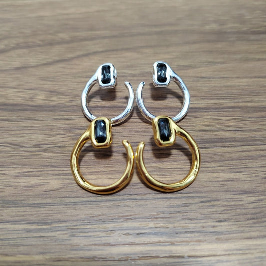 Needle-shaped earrings on neutral background. Alt: “UNOde50 Needle-Shaped Earrings – Sterling Silver-Plated Drops.”