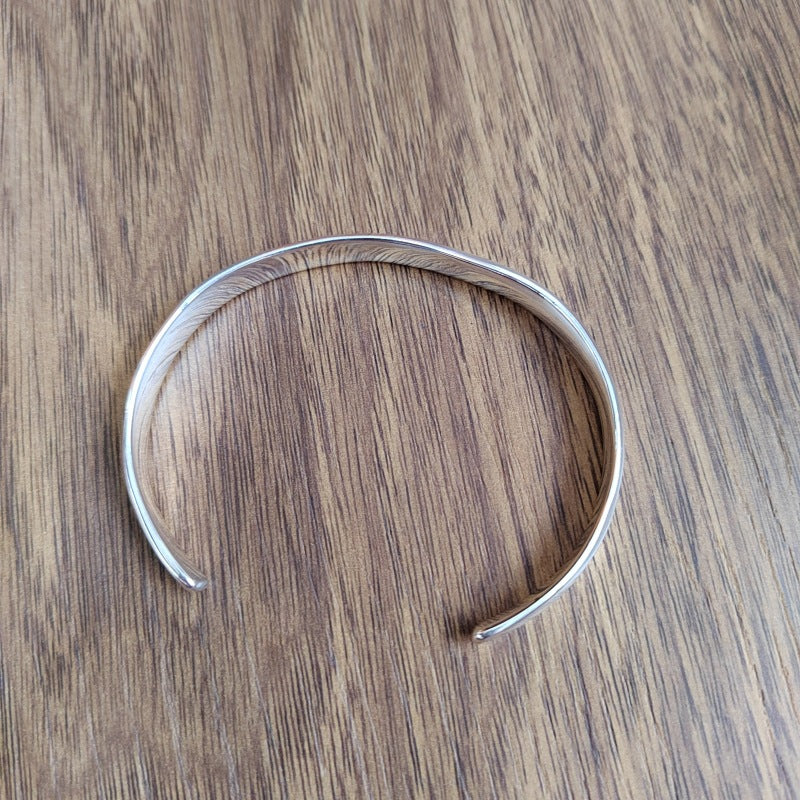 A polished silver-toned metal cuff bracelet with a hammered texture, displayed on a brown wooden surface.