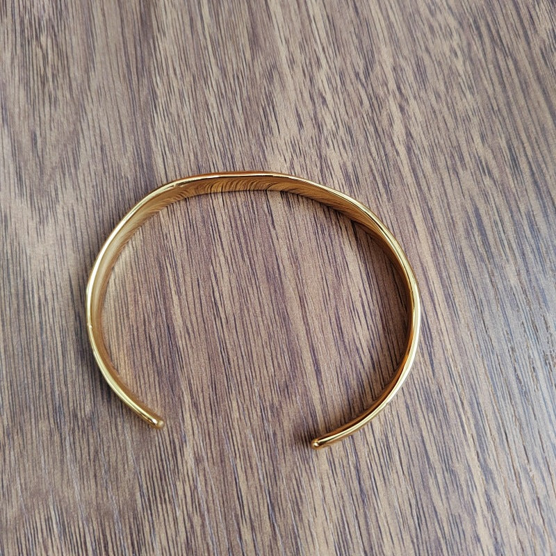 A polished gold-toned metal cuff bracelet with a textured, hammered finish, displayed on a dark brown wood grain surface.