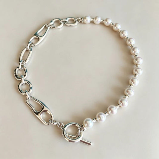 A silver-toned bracelet featuring a series of white pearl beads interspersed with polished oval links and a toggle clasp, displayed on a light beige background.