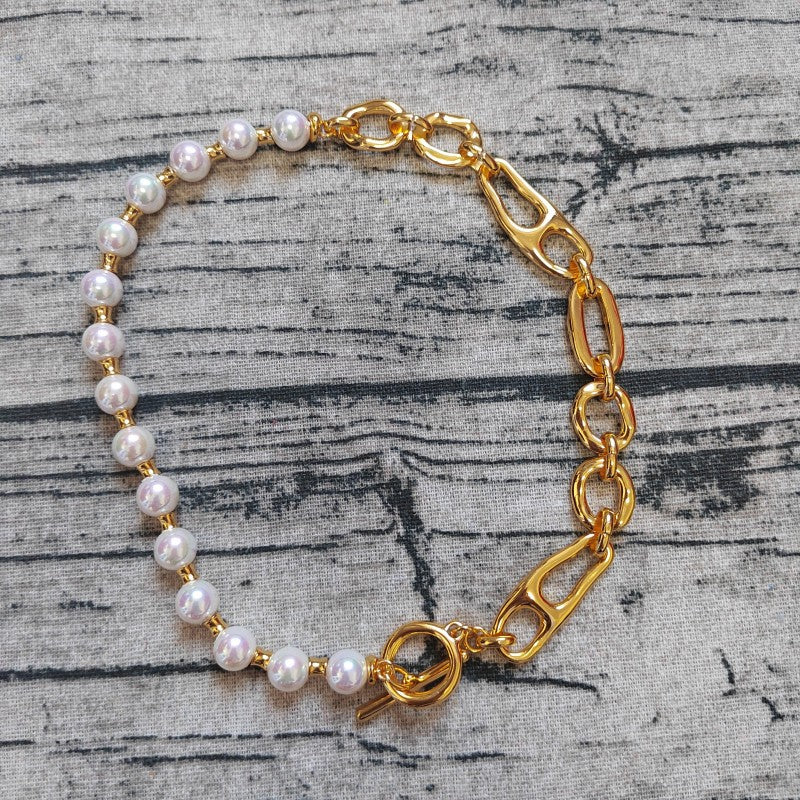 A gold chain bracelet with white pearl beads, displayed on a textured gray wood background.