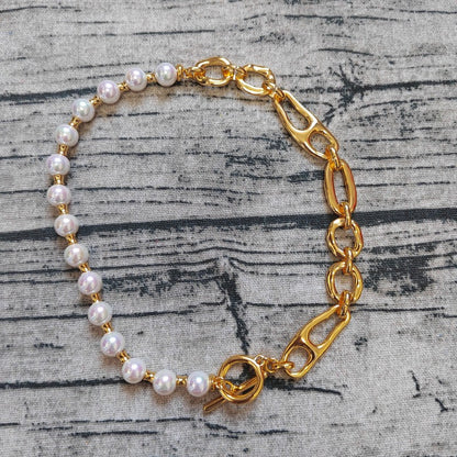 A gold chain bracelet with white pearl beads, displayed on a textured gray wood background.
