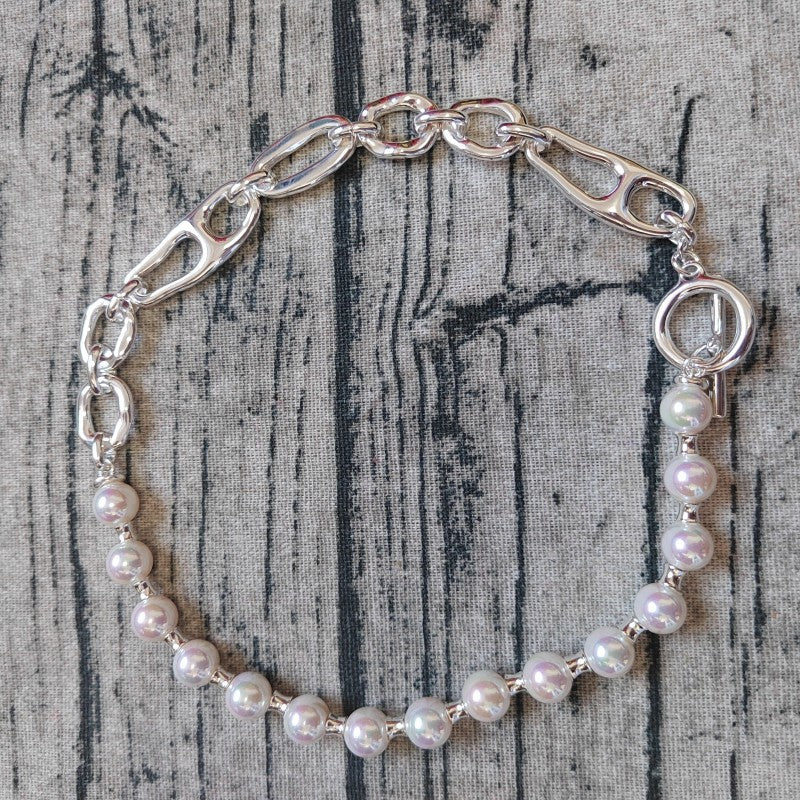 A silver-toned chain bracelet with a section of iridescent white pearl beads, displayed on a textured gray wood background.