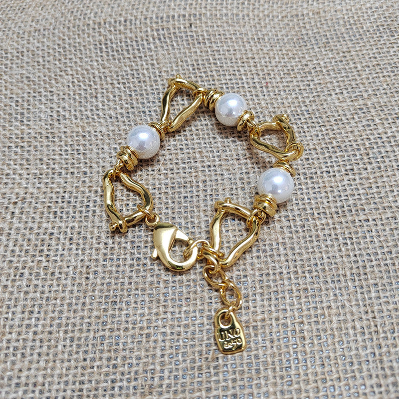 A gold-plated chain bracelet with three white pearl beads and a lobster clasp, displayed on a textured beige burlap background. A small tag engraved with 'JNDJ 925' is visible.