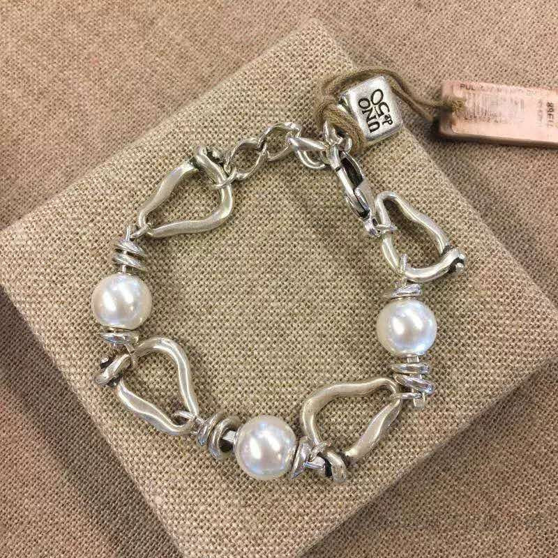 A sterling silver link bracelet with three white freshwater pearls, displayed on a textured beige fabric box. The bracelet features a combination of polished oval links, textured spiral-wrapped links, and a lobster clasp.