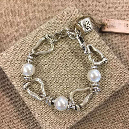 A sterling silver link bracelet with three white freshwater pearls, displayed on a textured beige fabric box. The bracelet features a combination of polished oval links, textured spiral-wrapped links, and a lobster clasp.