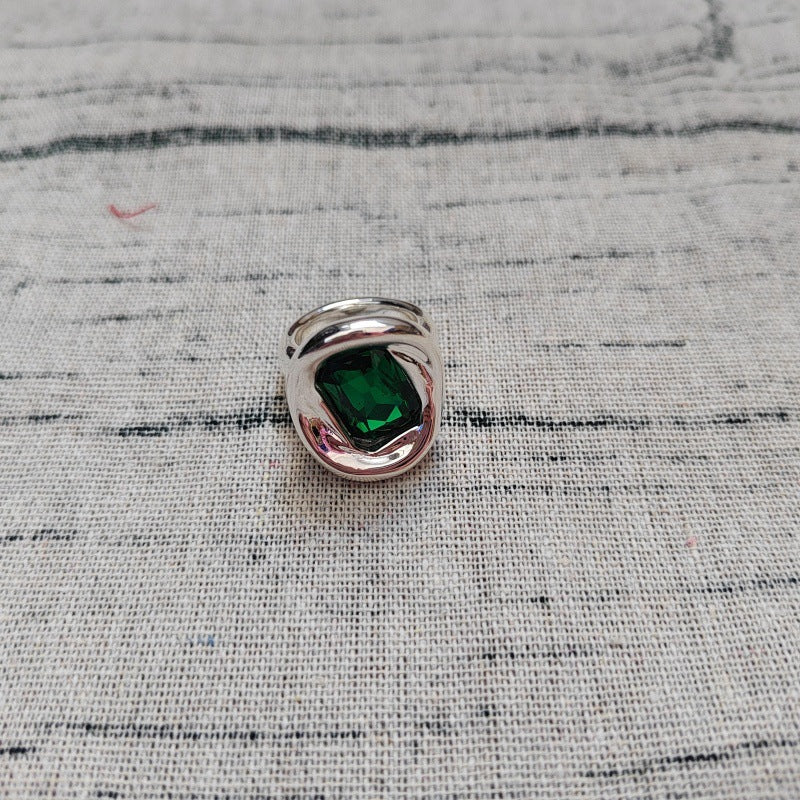 A silver ring featuring a square-cut green emerald gemstone, resting on a textured beige linen fabric background.
