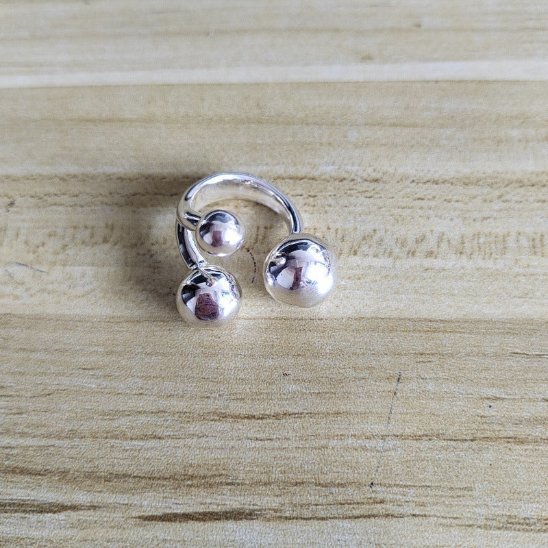 A silver-toned ring with two polished spherical beads, photographed on a light wood surface.