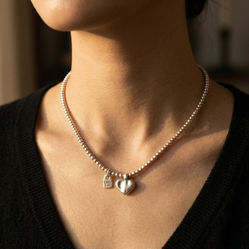 A close-up lifestyle shot of a model wearing a delicate silver beaded necklace with two heart-shaped charms, one engraved with 'I LOVE YOU'.