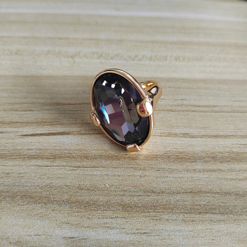 A rose gold ring featuring a large, faceted oval dark purple gemstone, resting on a light wood grain surface.