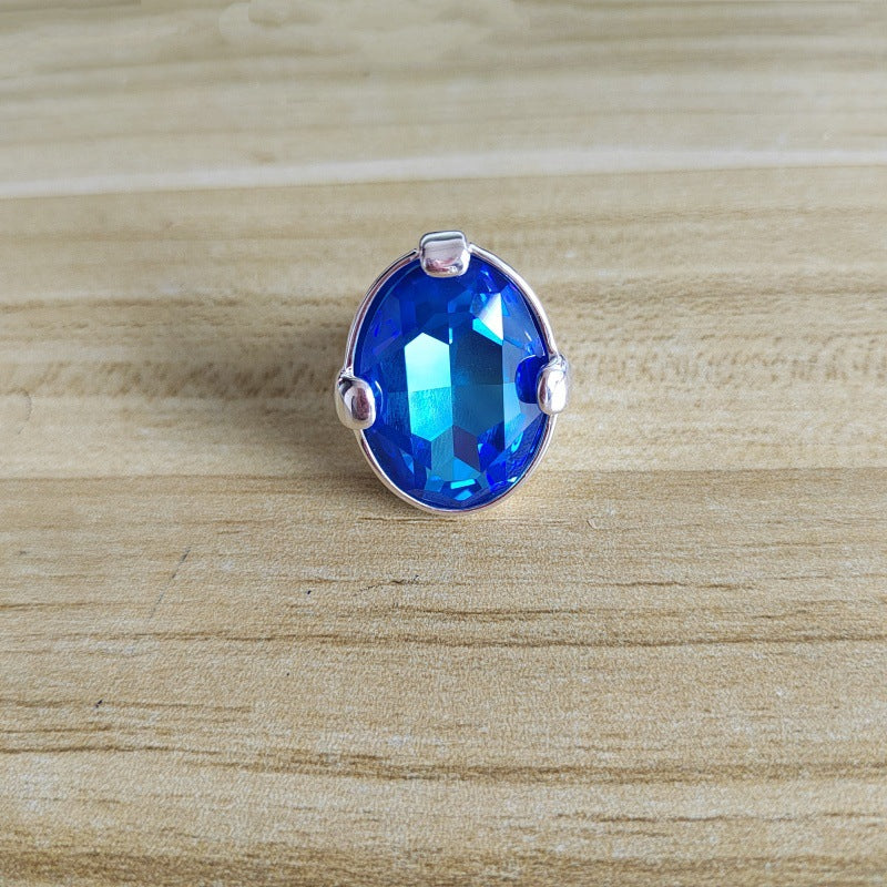 A silver ring featuring a large, faceted oval blue gemstone, photographed on a light-colored wooden surface.