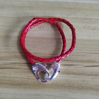 A red braided leather bracelet with a polished silver lobster clasp, displayed on a light wood grain surface.