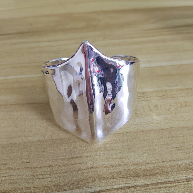 A polished silver ring with a unique, sculptural, faceted triangular top, resting on a light wood grain surface.