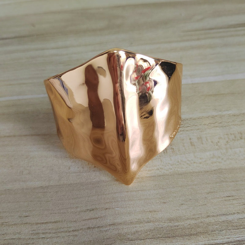 A hammered rose gold ring with an organic, wavy geometric shape, resting on a light wood grain surface.