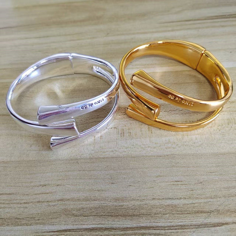 Two wrap-style cuff bracelets, one silver-toned and one gold-toned, displayed on a light wood surface. The silver bracelet is engraved with '925 sterling'.