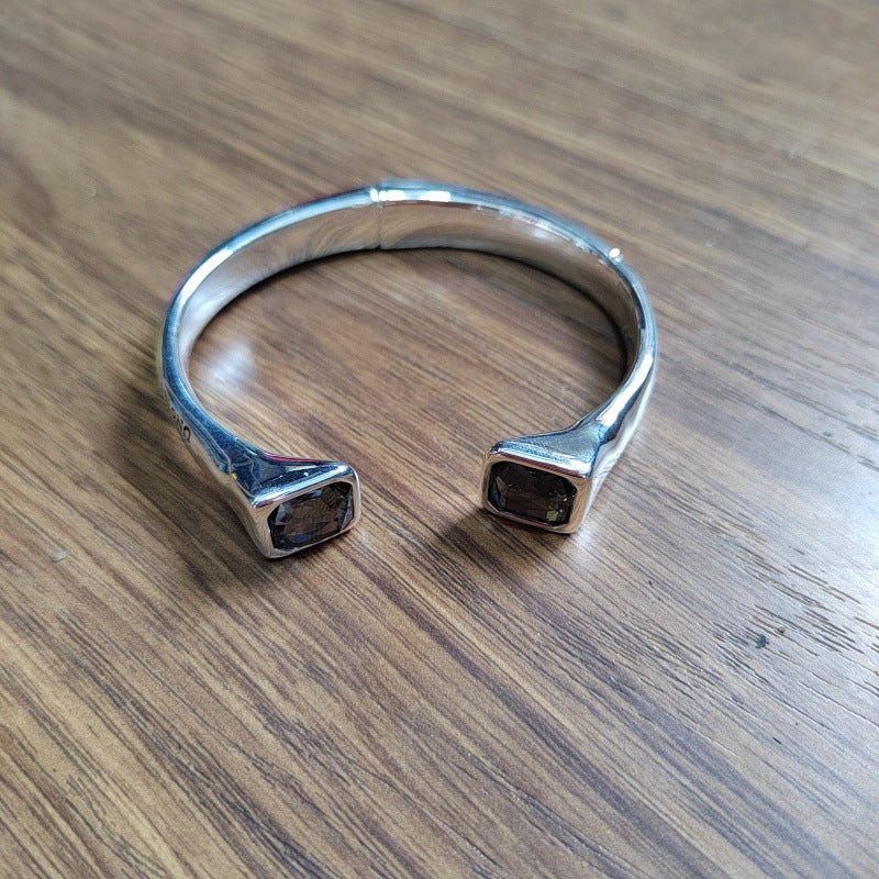 A polished silver cuff bracelet with two square bezel-set dark smoky gemstones, resting on a brown wooden surface.