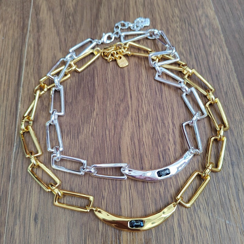 A two-tone chain link bracelet with gold and silver metal links, displayed on a brown wooden surface. The bracelet features a curved gold bar at the bottom with a small black rectangular inlay, and a polished silver bar with a matching black inlay.