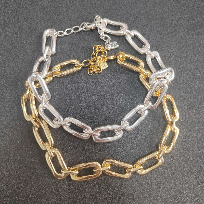 A two-tone chain link bracelet featuring alternating polished gold and silver paperclip-style links, displayed on a dark gray textured background.