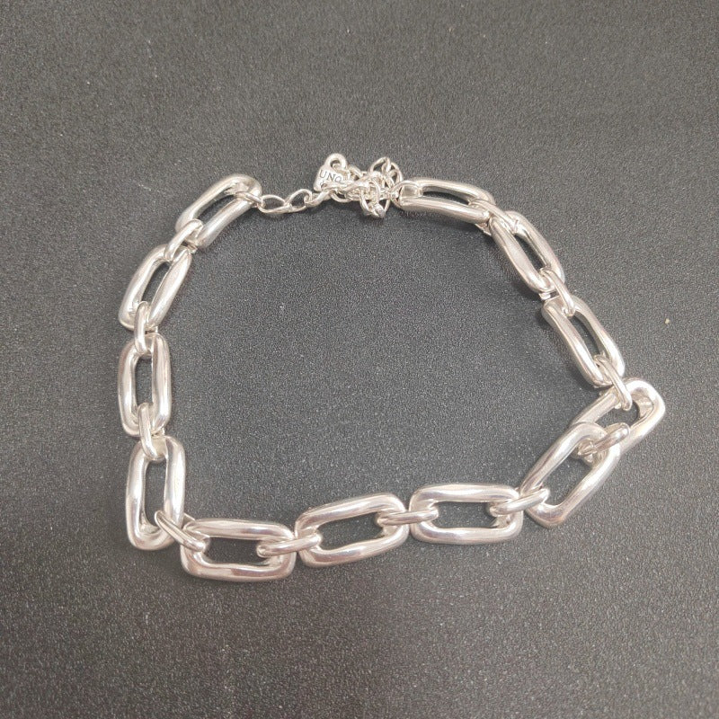 A silver chain link bracelet with thick, polished oval links, displayed on a dark gray textured background.