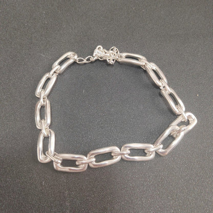 A silver chain link bracelet with thick, polished oval links, displayed on a dark gray textured background.