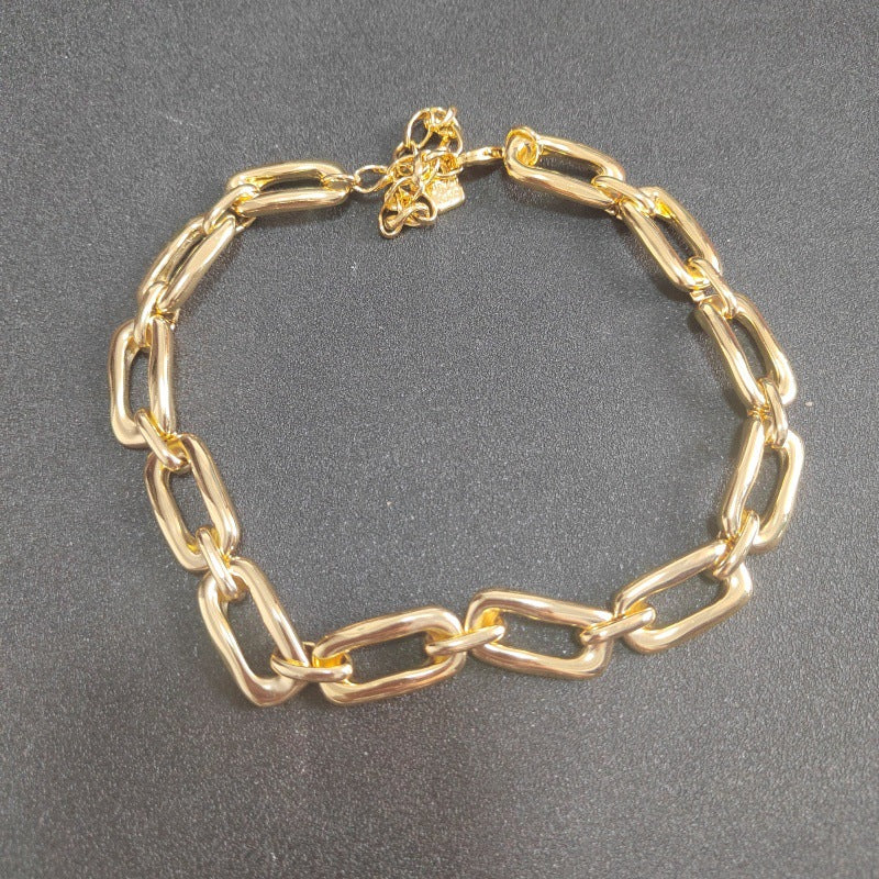 A gold chain link bracelet with oversized polished links, displayed on a dark gray textured background.