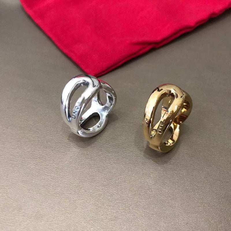Two interlocking knot-style rings, one silver and one gold, displayed on a textured gray surface with a red velvet pouch in the background.